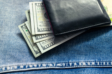 Black leather wallet with money. Dollar bills in a leather purse on a denim background