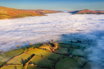 Aerial view of a fog filled valley surrounded by rural farmland in afternoon sunshine (Brecon...
