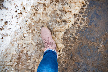 Foot in beige boot and blue jeans stepping on dirty snow