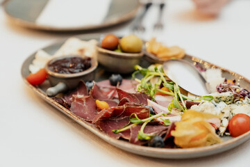 Various snacks mix: ham, blue cheese, tomato, olives, sauces. Wine appetizer in big plate on a table.
