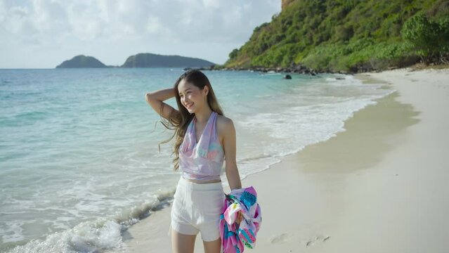 Beautiful Asian woman tourist walk on the beach happily having fun on a sunny summer vacation.