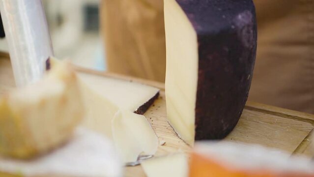 Seller in black gloves is cutting the cheese. Process of cutting cheese into small pieces for tasting. Dairy product sales concept