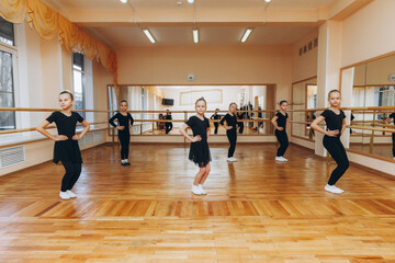 Girls 8 years old in black suits are doing choreography in a ballet class.