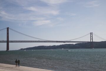 25 April Bridge and one couple walking by Tejo River at Lisbon