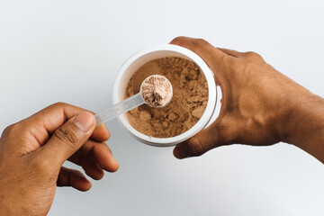 hands holding a scoop of chocolate protein over white background.