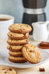 Homemade cookies with chocolate chunks and peanut butter.  A stack of biscuits in a white plate, a coffee pot and a cup on the table. Selective focus, copy space