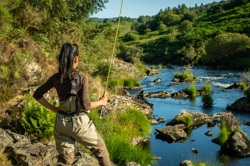 An asian female fly fisher women wearing waders and holding a rod