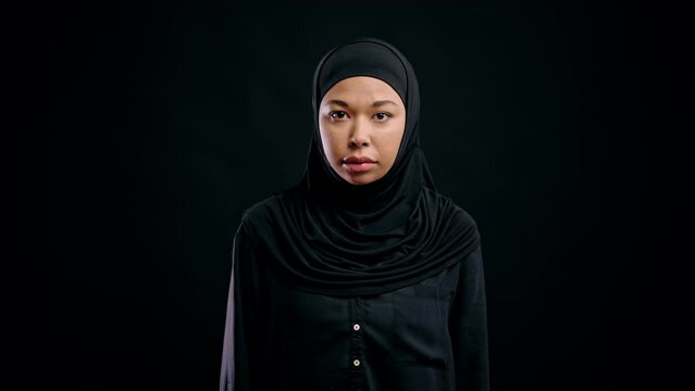 Serious muslim woman looking on camera against black background, women's rights