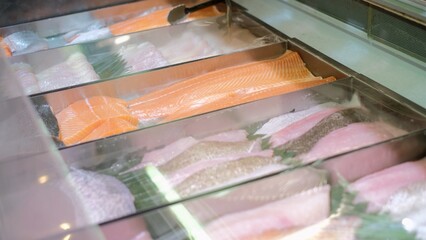 Supermarket's showcase full of assorted fresh fishes sliced fillets, display with marine sea products 