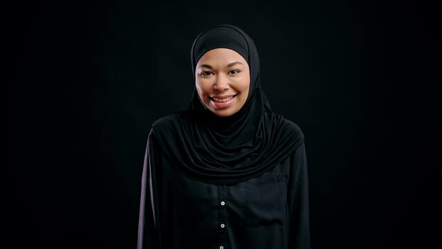 Happy muslim woman in traditional hijab smiling against black background freedom