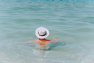 Fototapeta na wymiar a man in a white hat is bathing in blue sea water. A young man is resting in clear sea water
