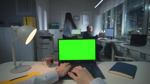 Pov shot of businessman typing on laptop with green screen late in office