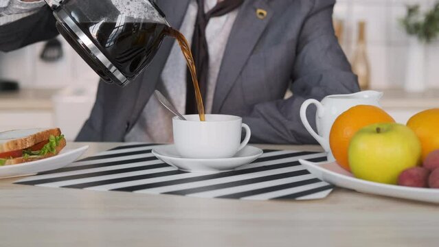 Close-up of Man Entrepreneur Pouring Coffee while Having Breakfast at Home. Coffee Spills over the Rim of the Cup. Business, Lifestyle, Overworking Concept