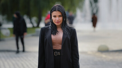 Young confident serious hispanic businesswoman in business suit standing outdoors near roadway pedestrian crossing girl leader employee manager office worker model posing sternly looking at camera