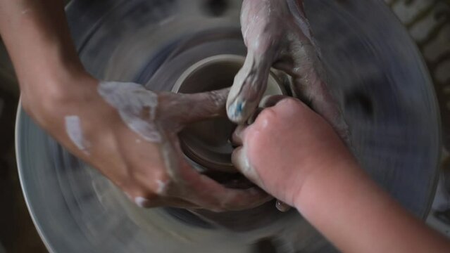 Pottery handcraft art lessons for small children, close up of adult hands helping, teaching a kid pottery
