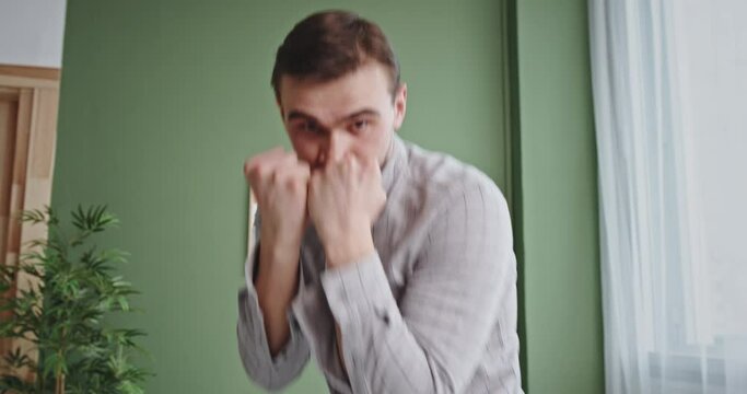 Determined man punching at camera. Active focused male boxer practicing punches while fighting and looking at camera at home