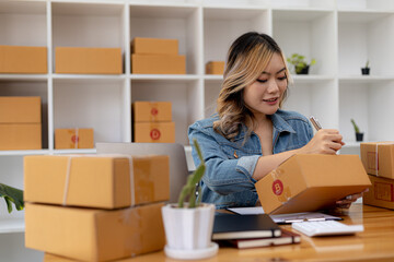 Woman who runs an e-commerce business is writing a list of customers on paper before shipping to them, she runs an e-commerce business on websites and social media. Concept of selling products online.