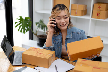 Asian woman is talking on the phone with a customer to confirm an order, she owns an online store, she packs and ships through a private transport company. Online selling and online shopping concepts.