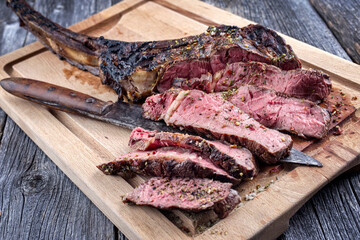 Traditional barbecue wagyu tomahawk beef steak with spice and herbs sliced and served as close-up on a rustic wooden board