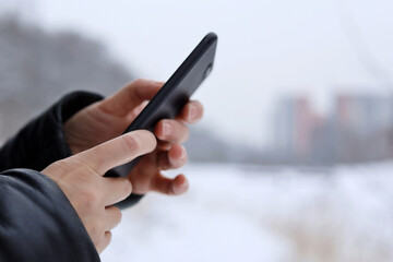 Female hands with smartphone close up on blurred background. Woman using mobile phone stands on a city street in snow winter