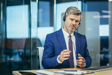 Businessman in a business suit looks at the webcam, uses a headset for video communication,...