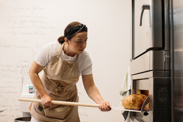 Female baker using a peel to take out a loaf of bread of the oven in a bakery