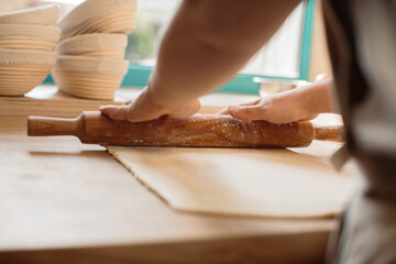 Woman hands rolling out dough in flour with rolling pin in bakery.