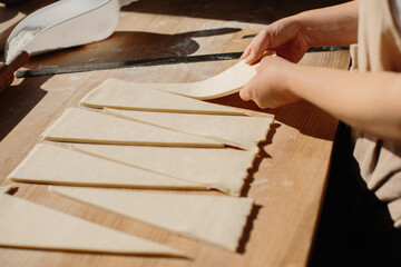 Woman baker cuts the dough into triangles for croissants. Making croissants in the bakery.