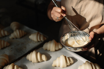 Female baker smears raw croissants with a brush in the yolk, the cooking process.