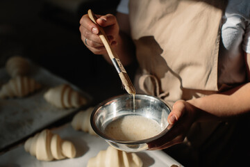 Female baker smears raw croissants with a brush in the yolk, the cooking process.