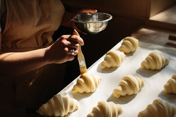 Female baker smears raw croissants with a brush in the yolk, the cooking process.