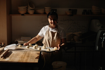 Female pastry chef holding baking sheet with uncooked croissants in kitchen