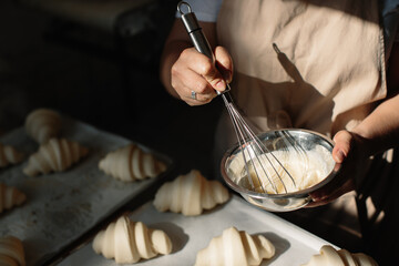 Female baker smears raw croissants with a brush in the yolk, the cooking process.