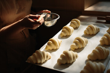 Female baker smears raw croissants with a brush in the yolk, the cooking process.