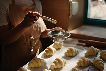 Female baker smears raw croissants with a brush in the yolk, the cooking process.