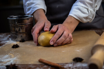There is a dough on the parchment, slightly sprinkled with flour, which the cook holds in his hands, a rolling pin, cookie cutters, cinnamon and a metal flour jar are visible around. High quality