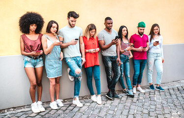 Multicultural milenials using smartphone against wall at university college backyard - Young students addicted by mobile smart phone - Technology concept with always connected millenials - Warm filter