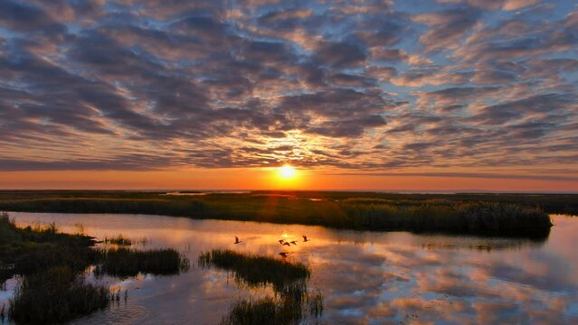 Incredible sunrise sky with textured clouds reflecting from tranquil waters below, aerial view.