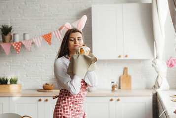 A beautiful young girl in rabbit ears holds an Easter cake in her hands, sniffs a pleasantly...