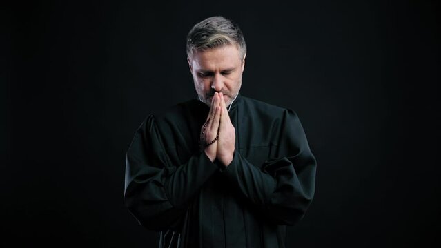 Catholic priest putting hands together to pray isolated on black background