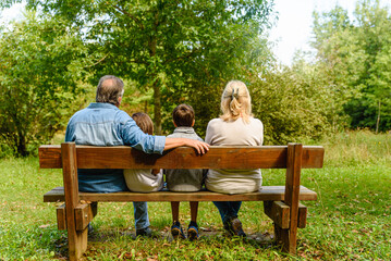 Children and grandparents sit together on wood bench in the park