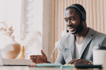 Young smiling african american man in headset consulting client customer via video call on laptop