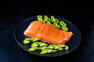 Salted fish salmon with pepper and onions on a black plate. Top view. Free space for your text.