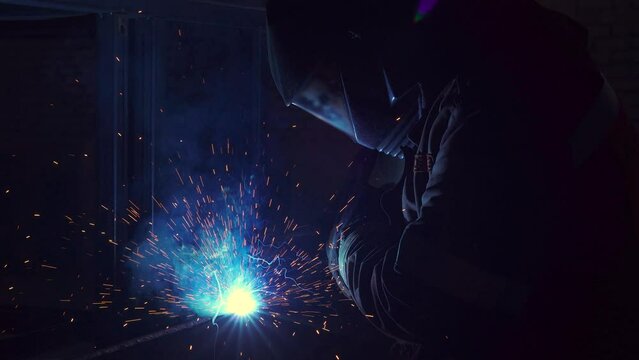 Half length of welder at work. Worker welds metal parts. Welding process, sparks, flame, smoke. 