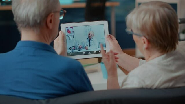 Senior Couple Attending Online Meeting With Doctor On Digital Tablet, Doing Remote Consultation At Home. Elder People Using Videoconference Call On Modern Gadget For Internet Telemedicine.