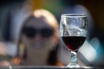 Glass of red wine on the front, defocused woman silhouette in swimming pool on the background