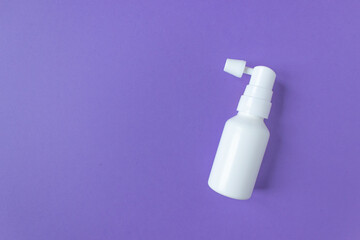 White ear spray bottle with nozzle on a purple background. Prevention and care of the ears. Space...