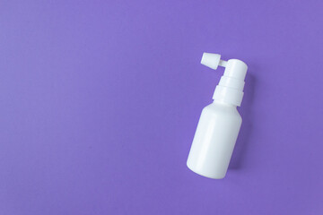White ear spray bottle with nozzle on a purple background. Prevention and care of the ears. Space for text.