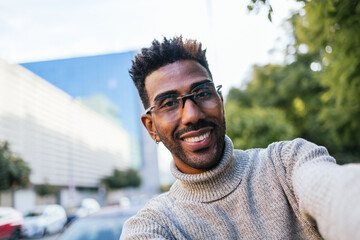 African American man in turtleneck vest and glasses taking a selfie in the city