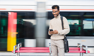 African American man in turtleneck vest and glasses using his mobile phone in a train station